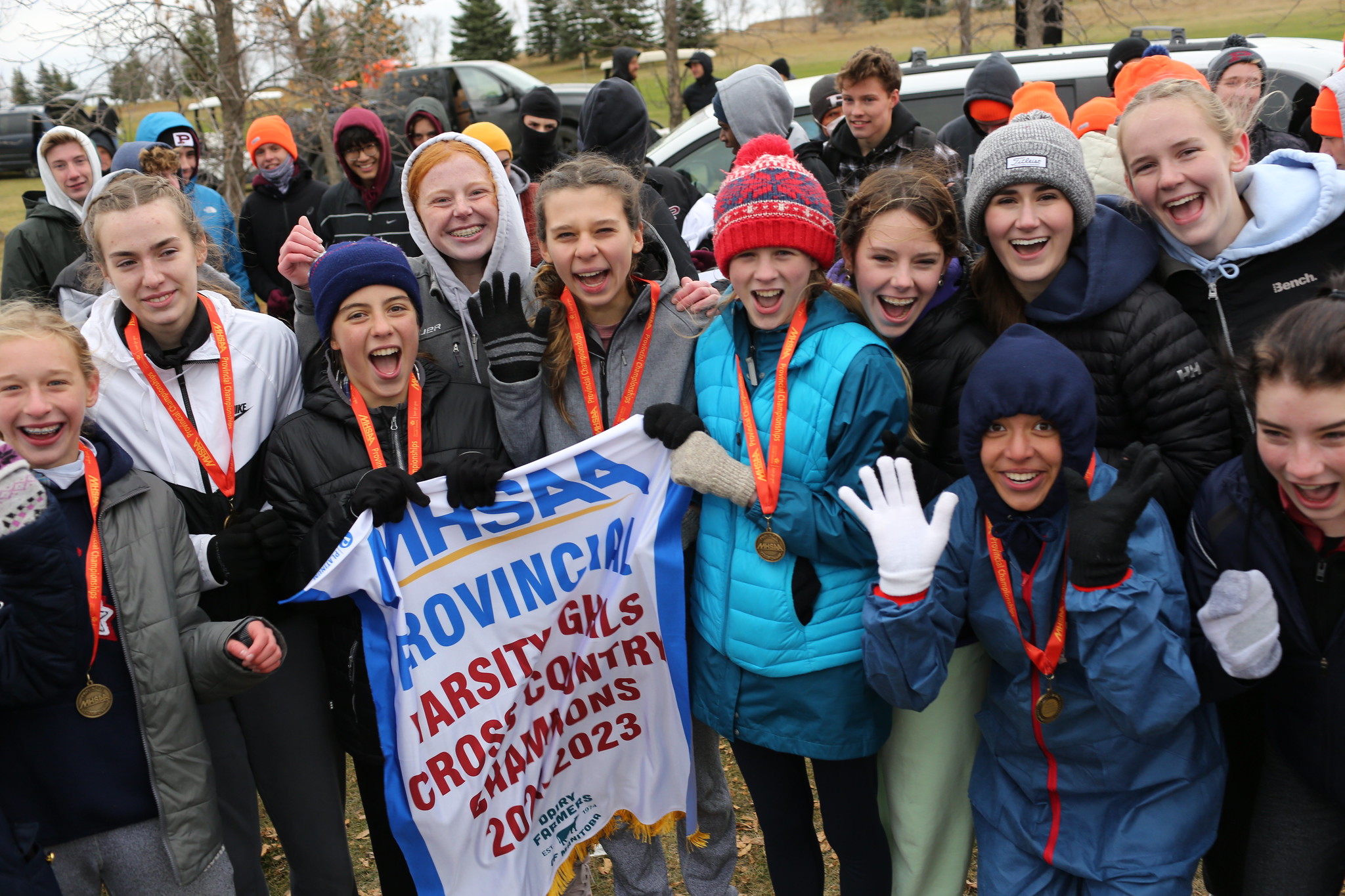 A group of excited students hold up a banner that reads 'Provincial Varsity Girls’ Cross-Country Champions 2022-2023'.