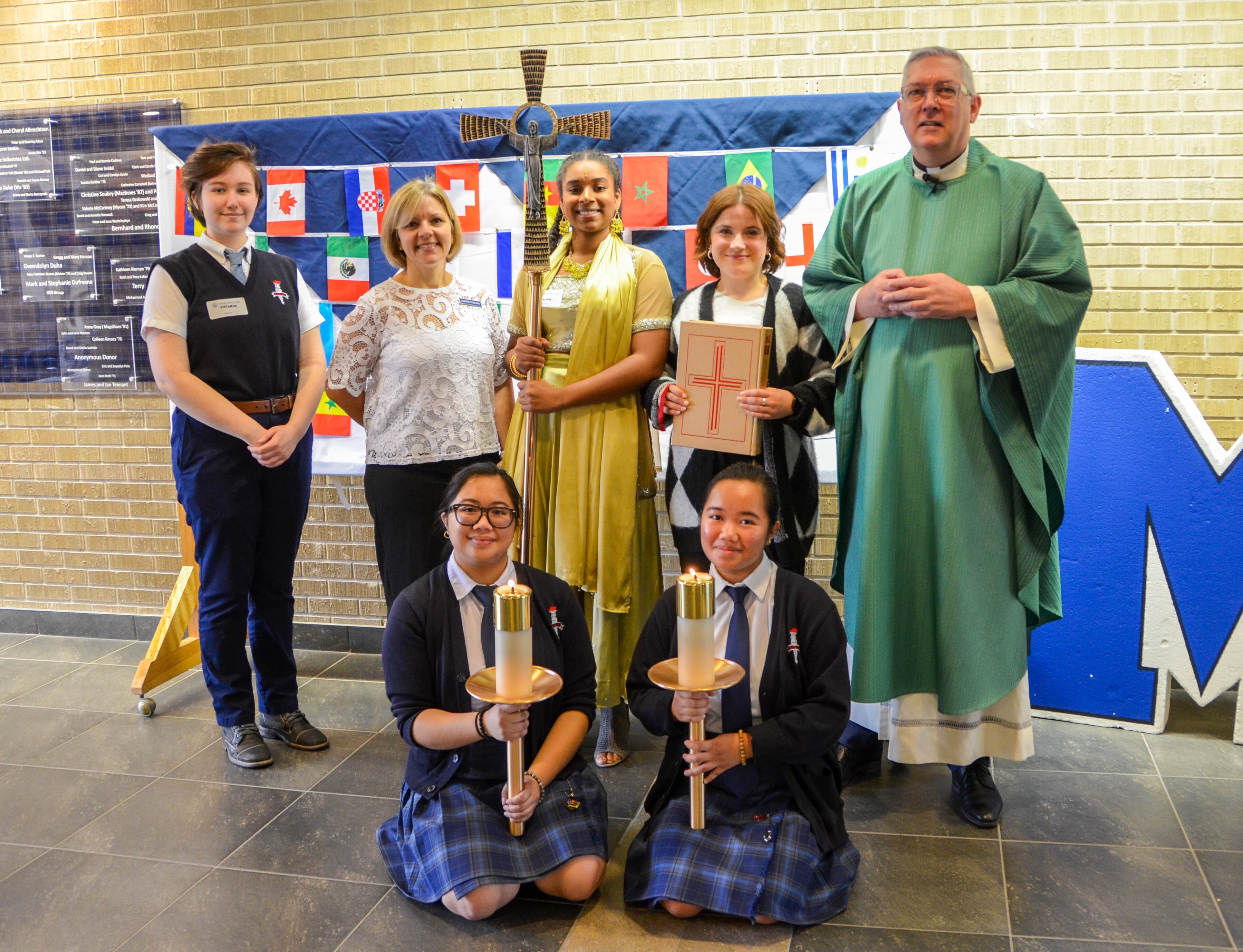 a group of women holding items used in mass celebration together with a priest wearing a green garment.