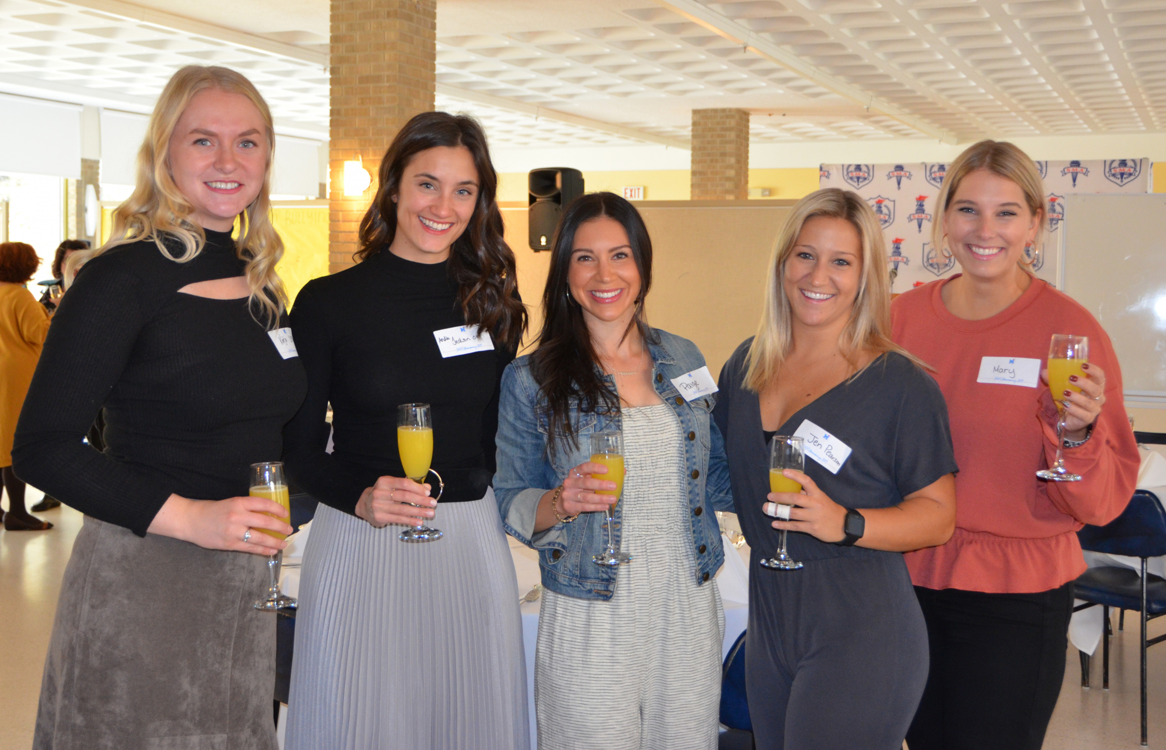 Five smiling St. Mary's Academy alumnae hold glasses with an orange beverage.
