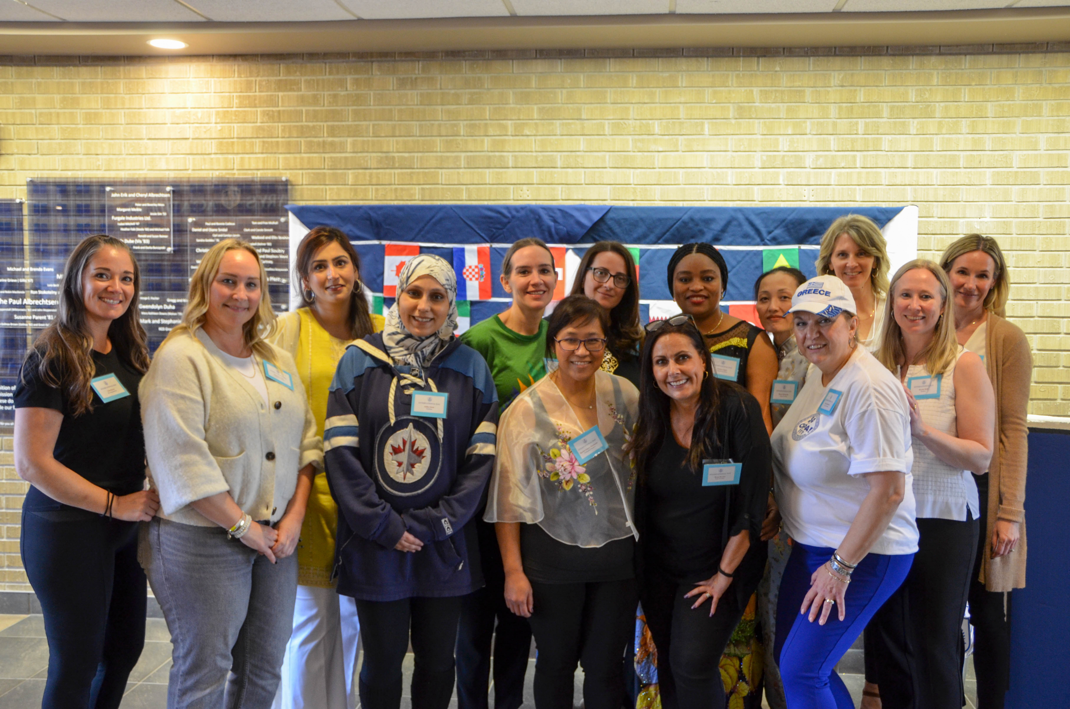 A group of parent volunteers with name tags stand in front of a quilt with different world flags on it.