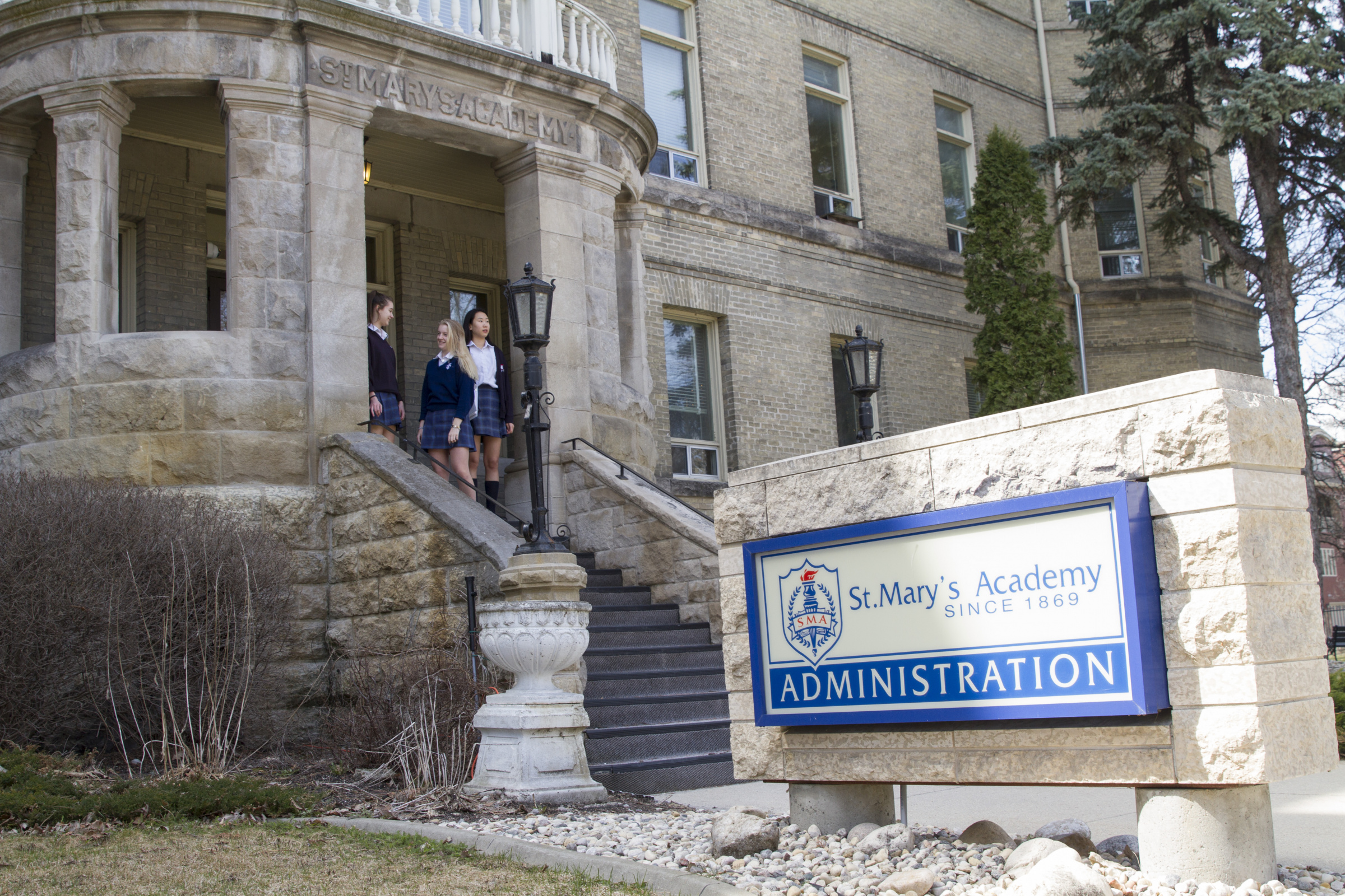 Three students walk out the St. Mary’s Academy doors, with the Academy’s Administration sign in the foreground.