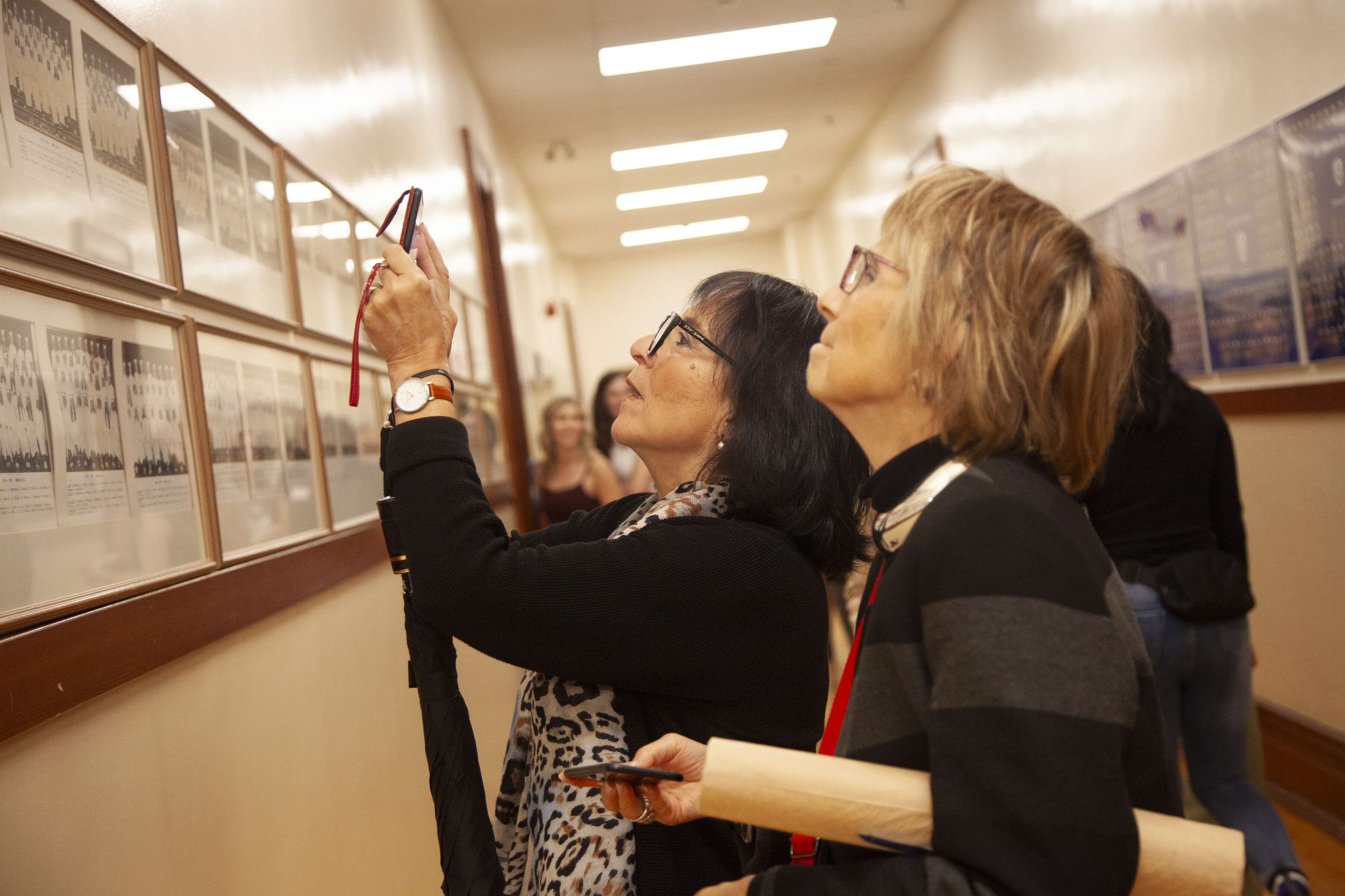 Two alumnae admire their school photos and take pictures in the hallway at St. Mary's Academy.