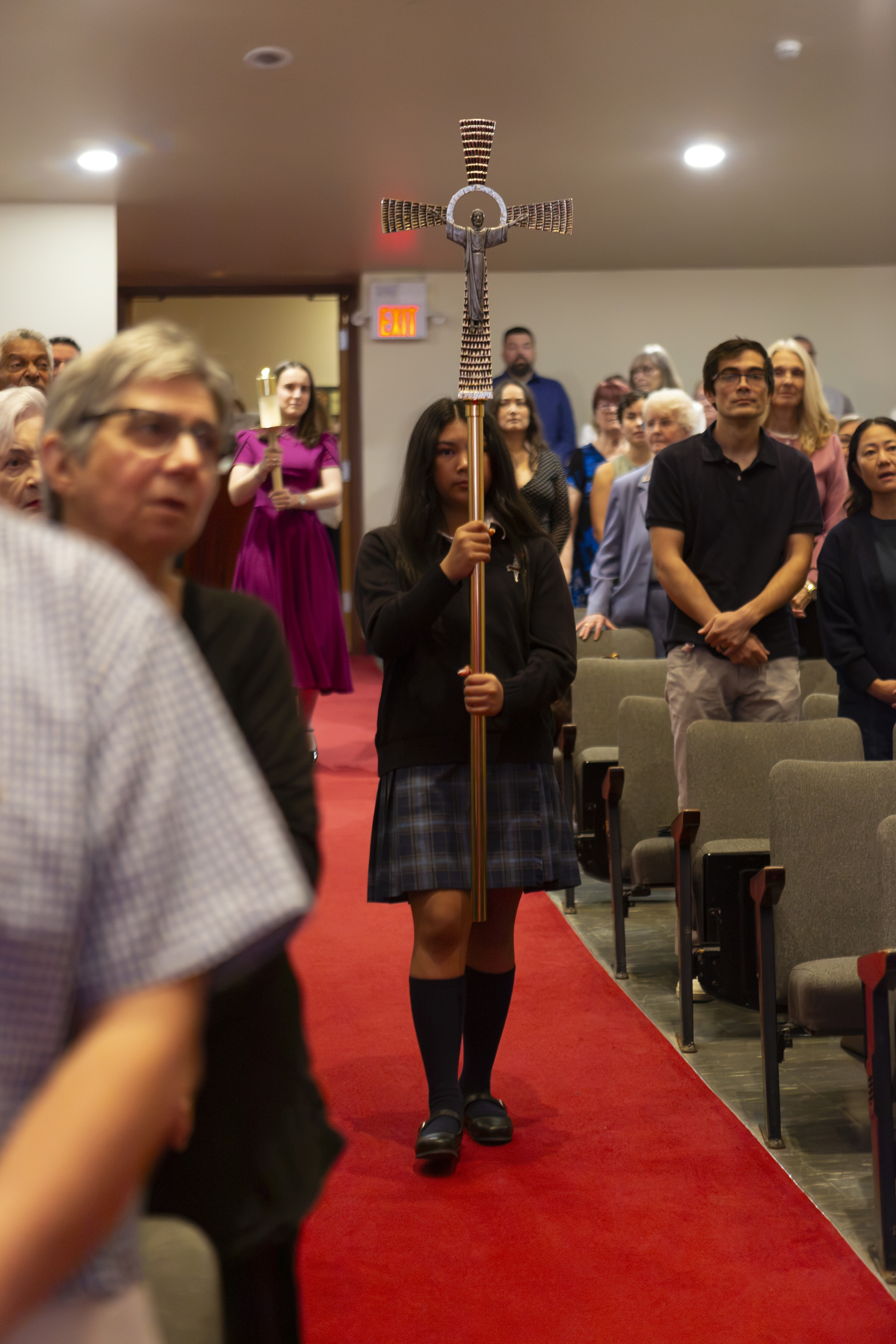 an SMA student holding a cross while walking down a theatre aisle.