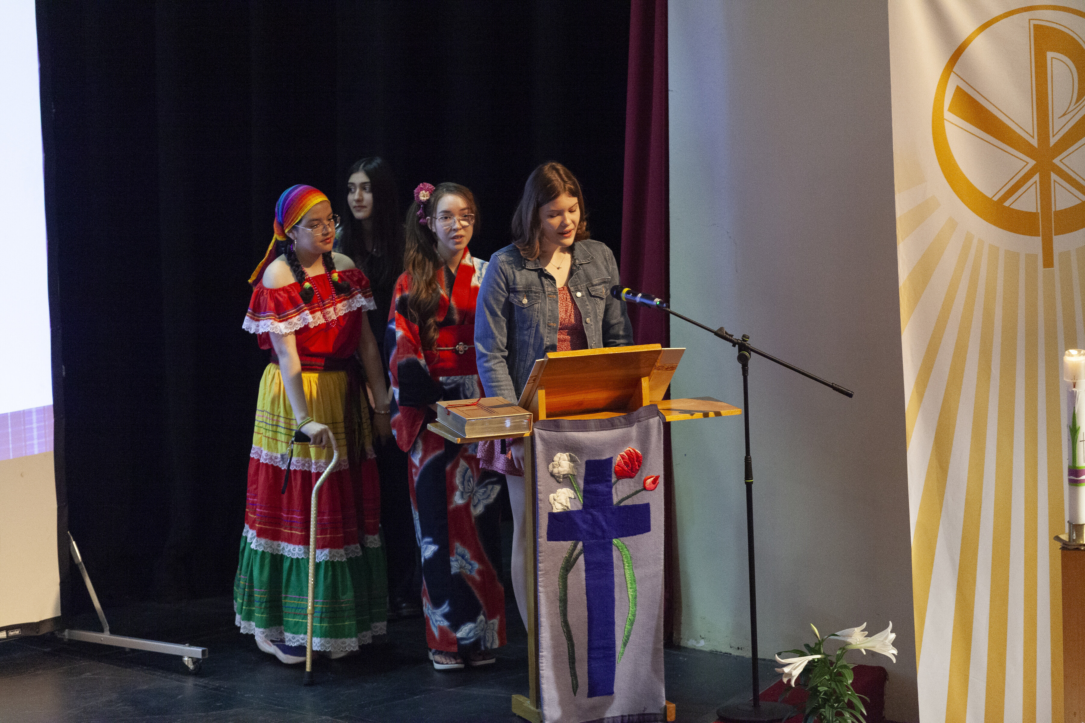 Three female students wearing cultural outfits standing in line with a podium in front of them
