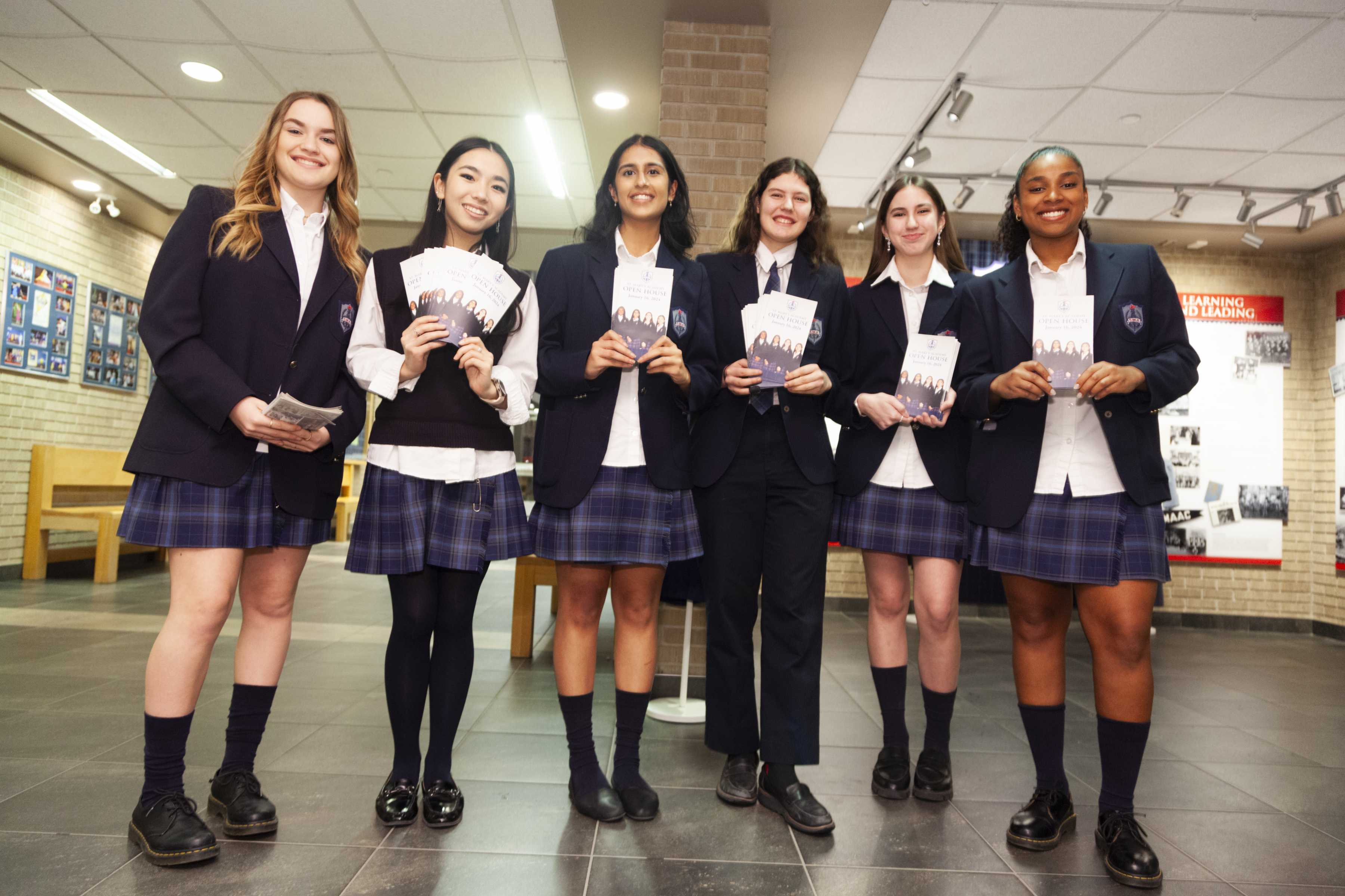 Six smiling St. Mary's Academy students hold up brochures advertising the school's Open House.