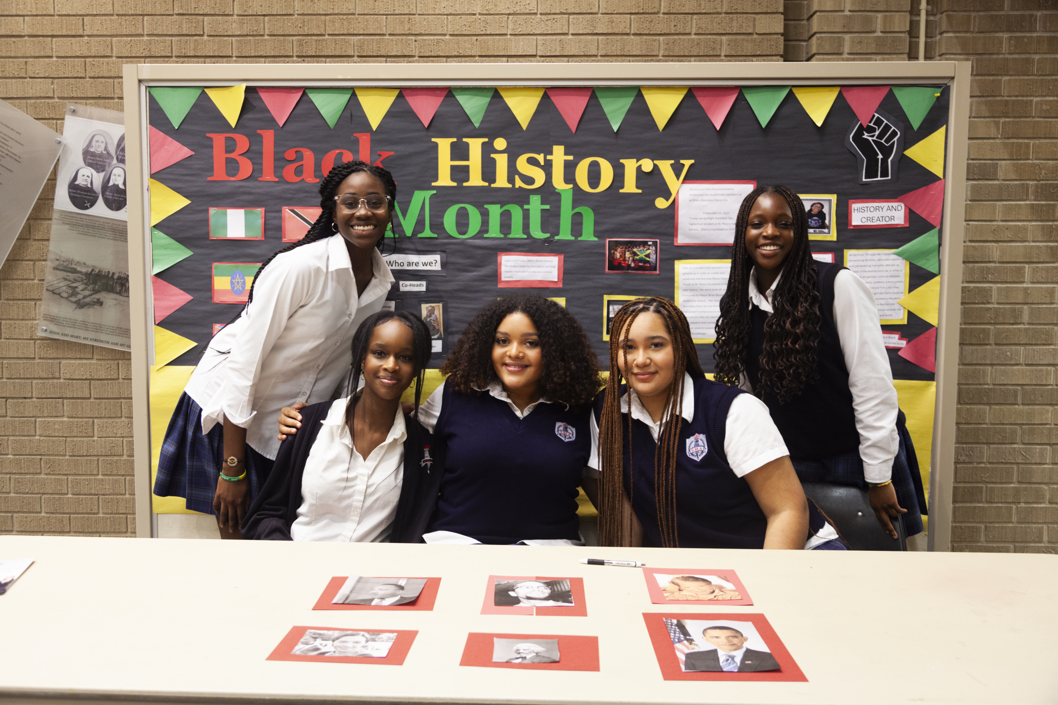 Five St. Mary's Academy students sit and stand in front of a Black History Month poster.