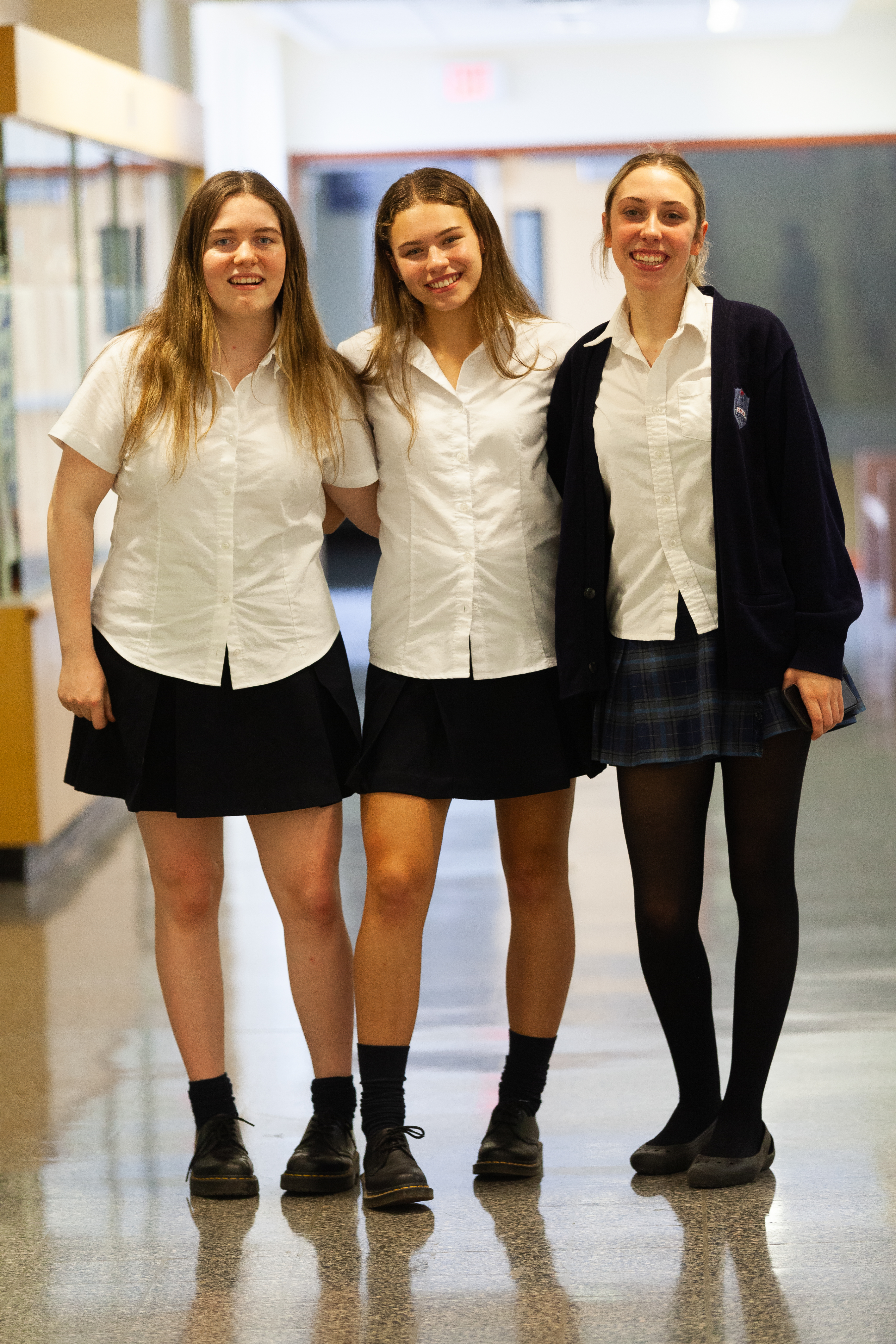 Three women in white button-down shirts smile.