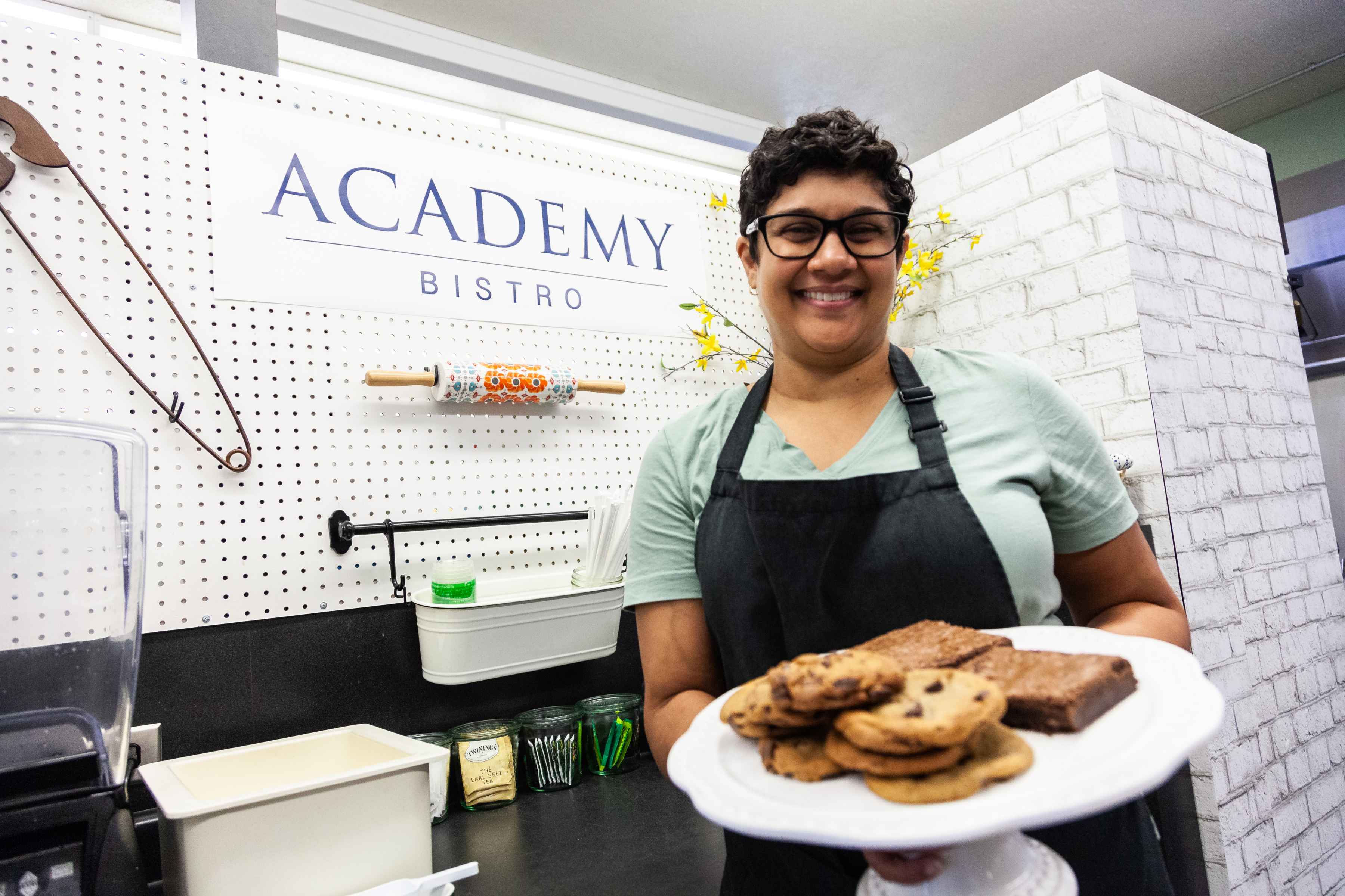 A smiling Academy Bistro team member holds a plate of cookies.