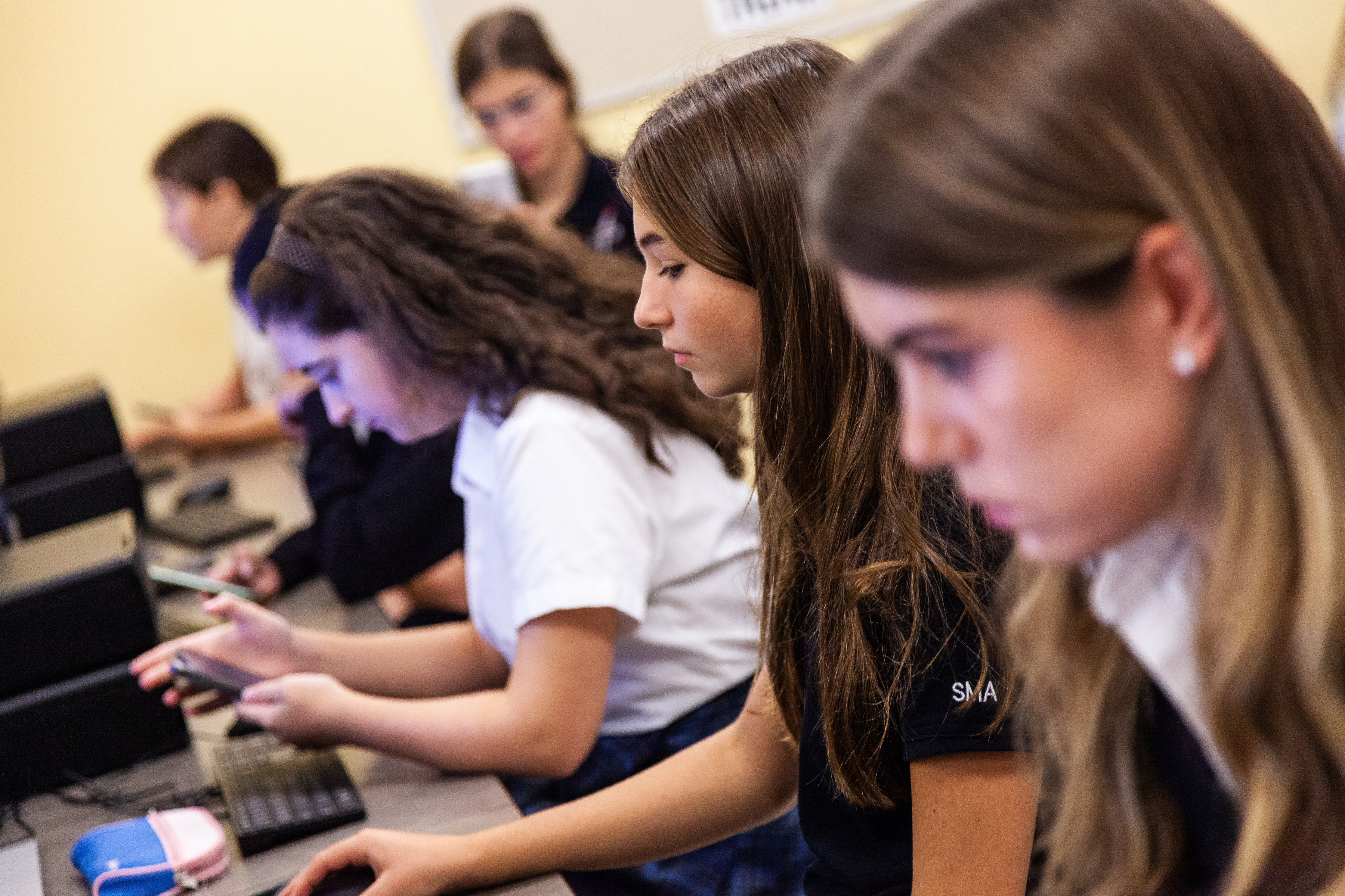 Several uniformed students concentrate while typing at computers.
