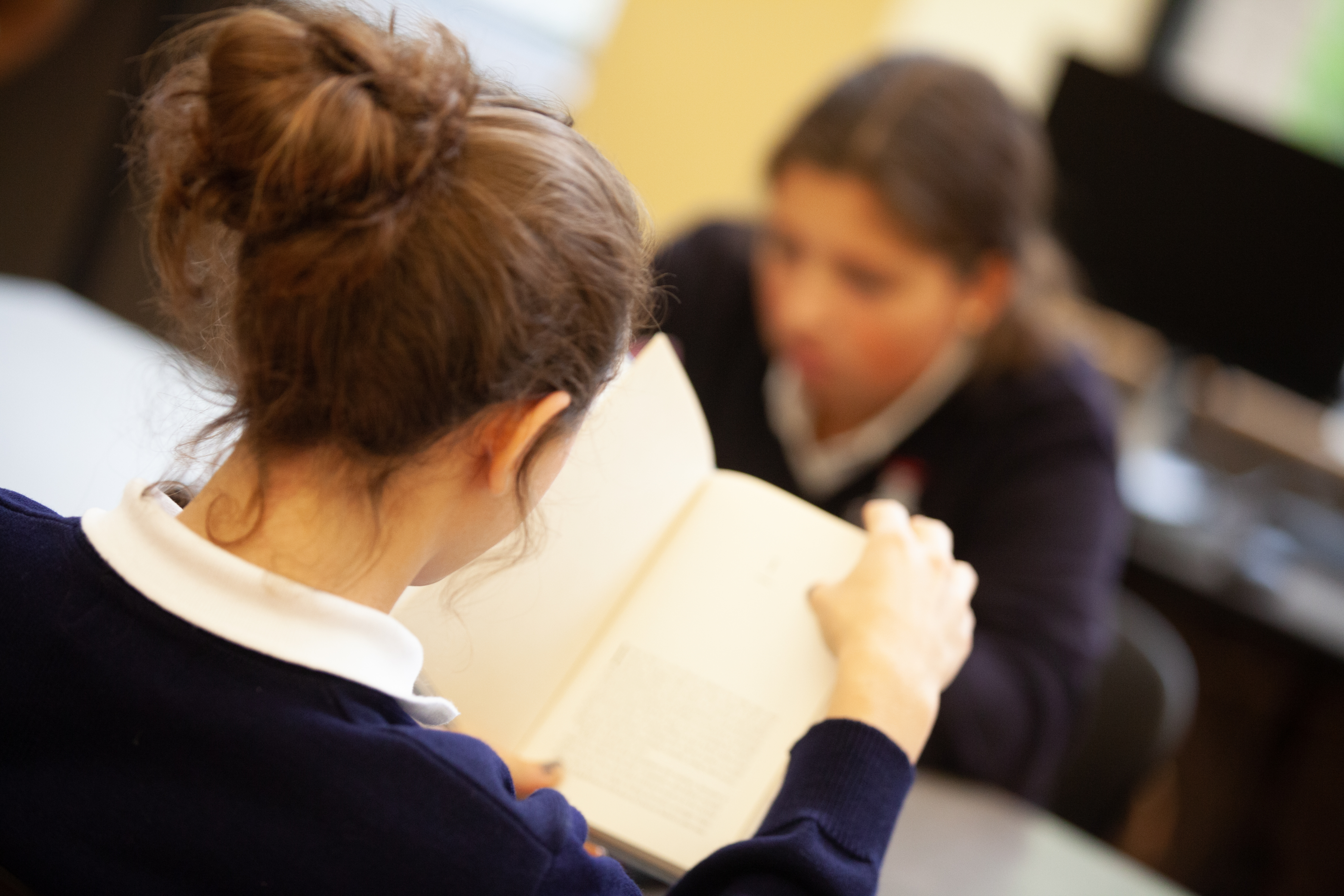 A St. Mary's Academy student flips a page in a book, with another student in the background.