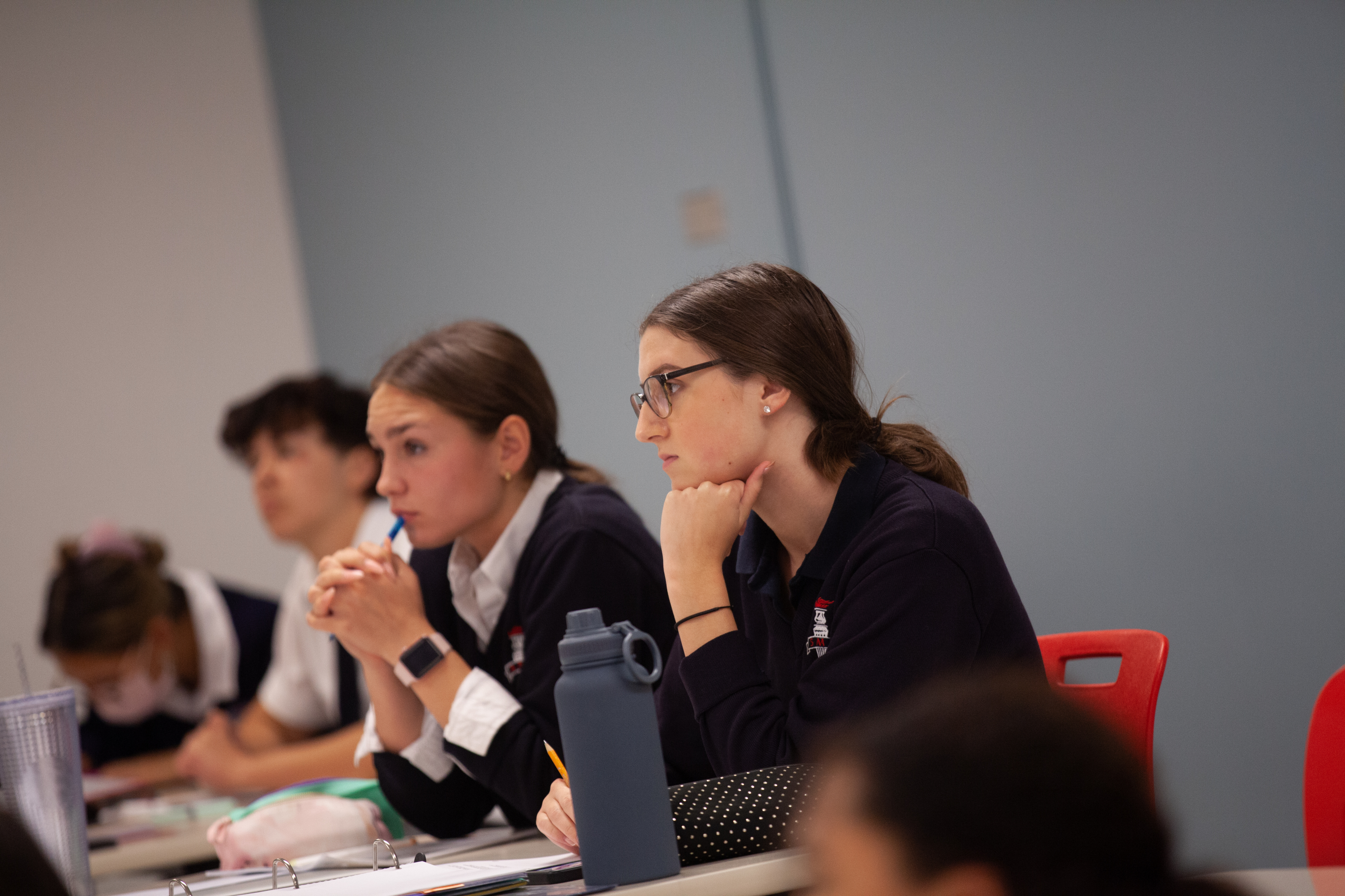 Uniformed St. Mary's Academy students listen and take notes while sitting in a classroom, with a waterbottle in the foreground.