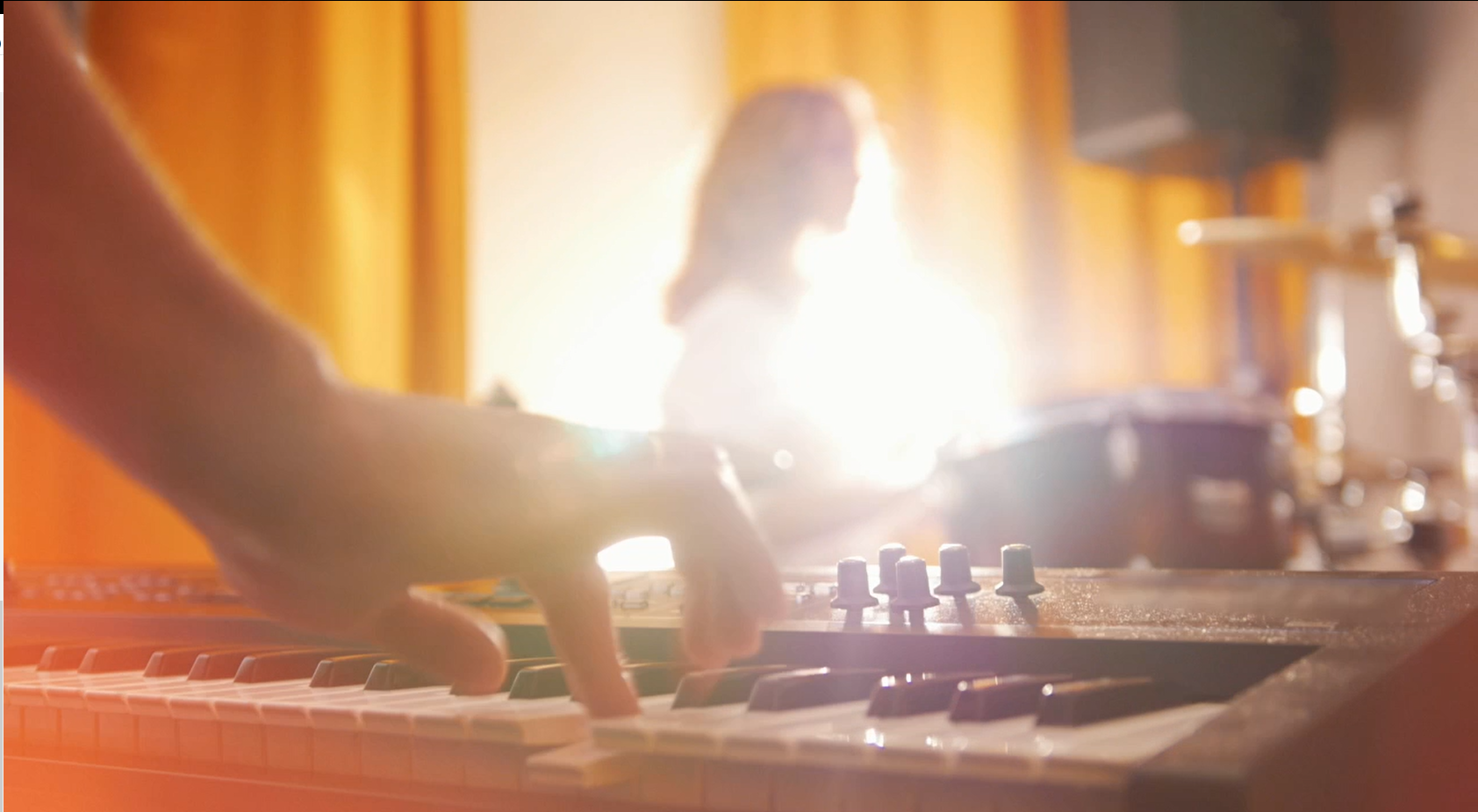 A hand presses keys on a keyboard, with a person out of focus in the background.