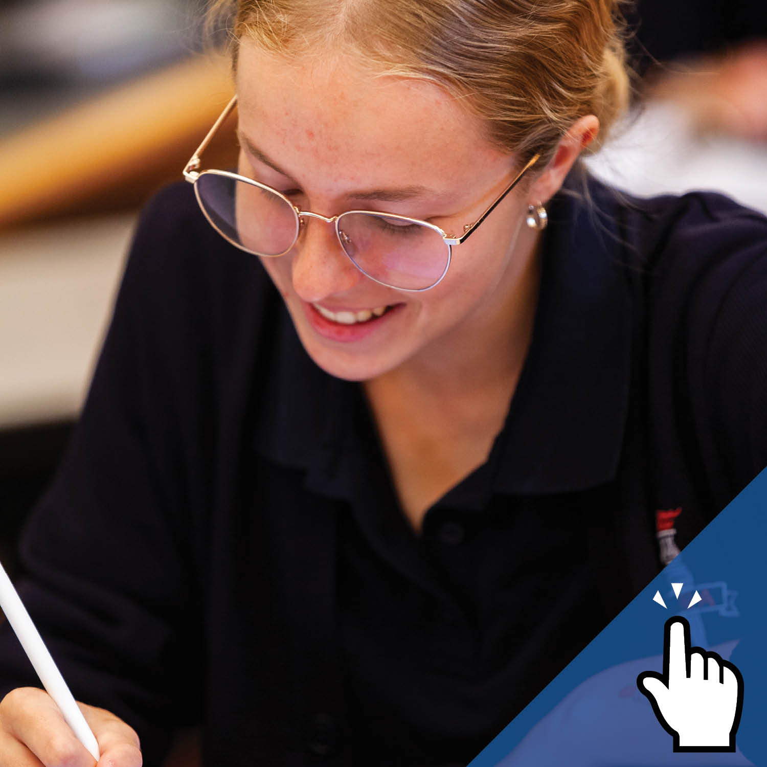 A smiling student wearing glasses writes.