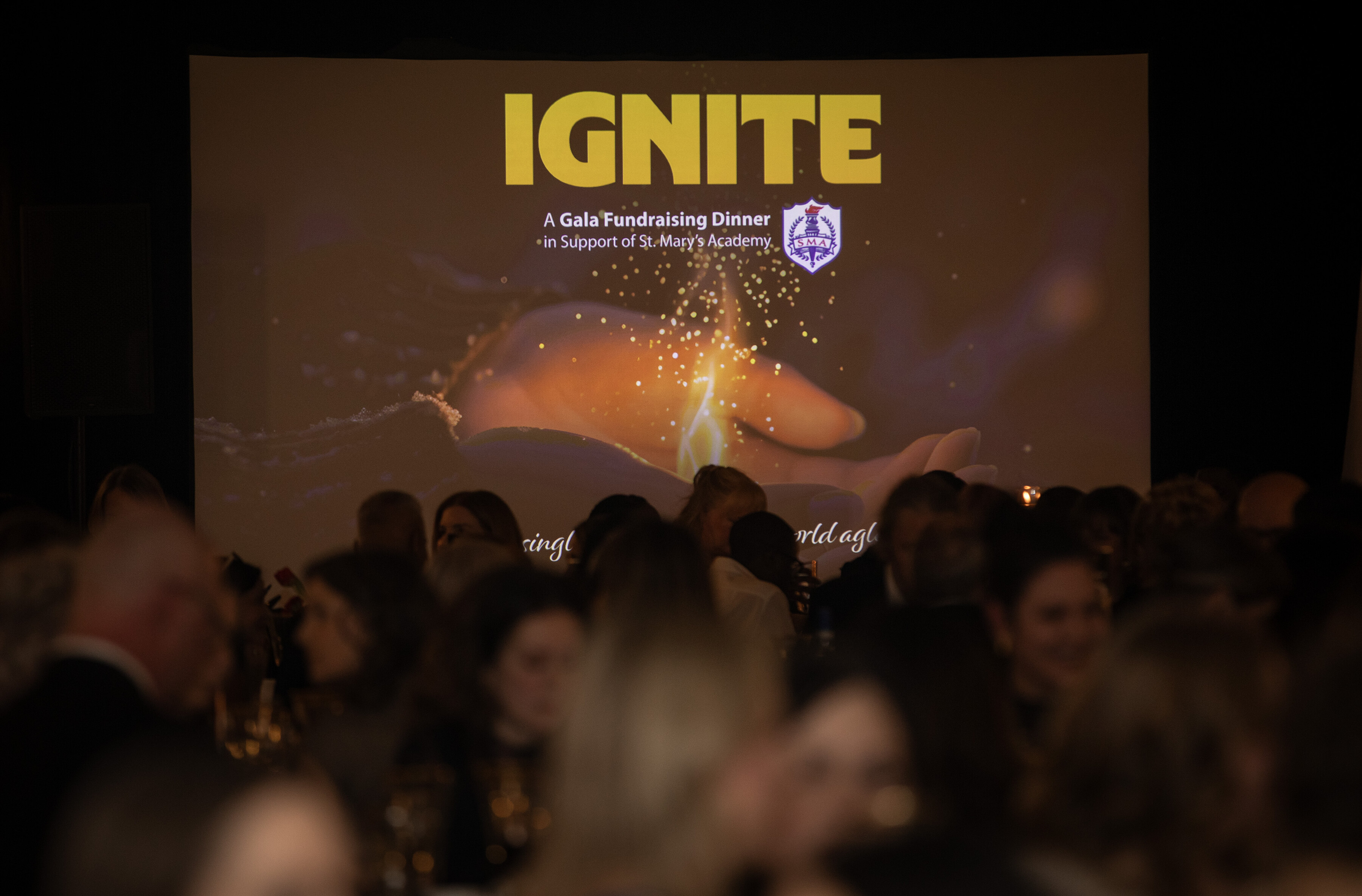 a group of people sitting and a projector screen in the background with a word that says "Ignite"