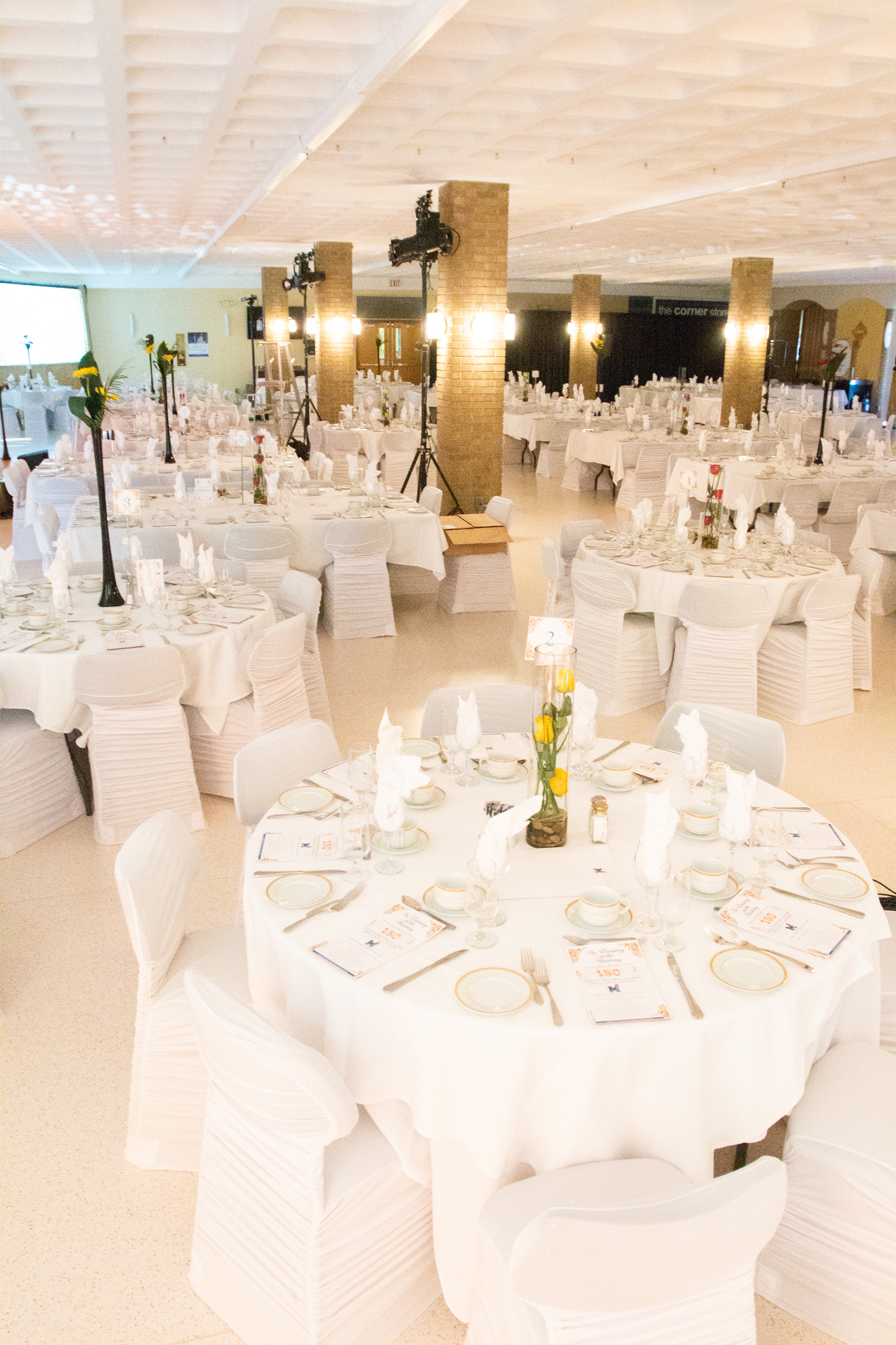 a dining hall filled with fancy white dining tables and chairs with fancy dinner table settings