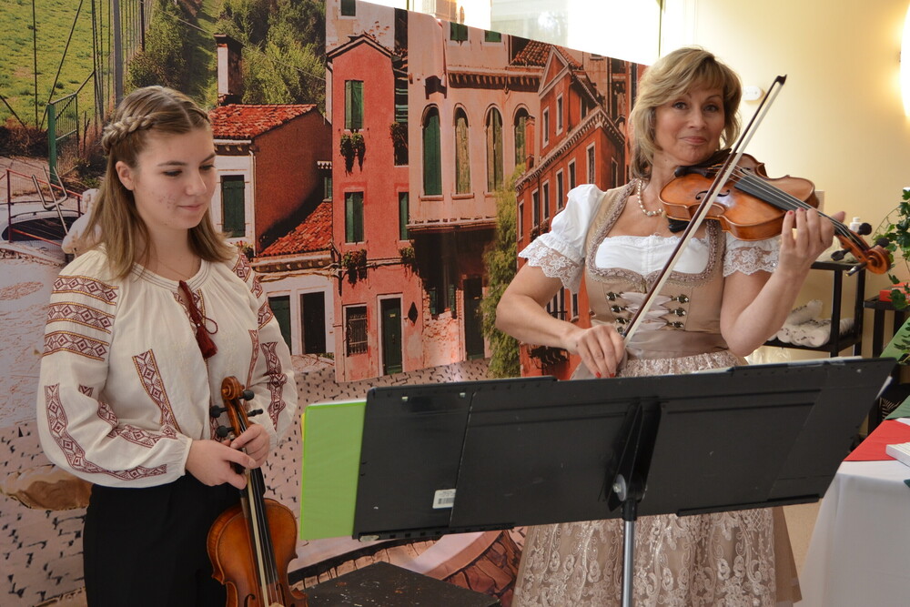 Two women playing violin in front of a scenic backdrop